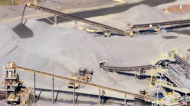 Aerial overview of conveyor belts and gravel piles with front loaders excavating and moving fill in quarry
