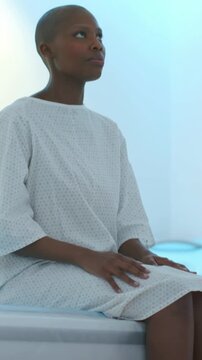 Vertical video: Looking lady in gown sitting on exam bed reacting to doctor entering in exam room