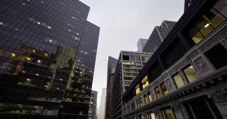 Fototapeta premium looking up in corporate canyon at dusk with reflective glass towers and warm office lights, narrow street perspective emphasizes scale and ambition, dynamic