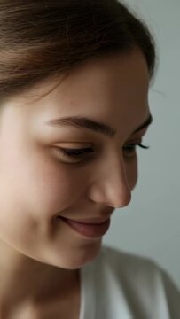 Vertical video: Smiling woman closing eyes and turning head after camera cue in studio in white top