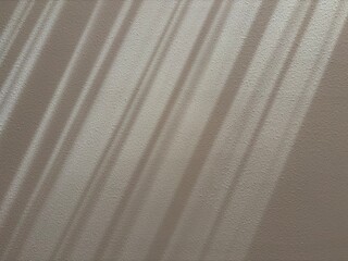 Fototapeta premium Soft window light shadow on a textured wall creating a minimalist abstract background with natural sunlight.