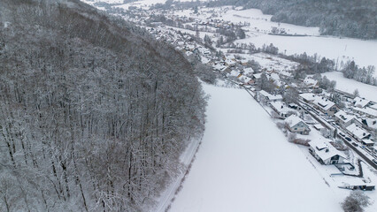 Aerial view of snowy village and frozen fields beside forest in winter Germany