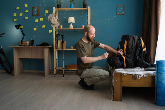 Bearded young man packing trekking backpack for hiking journey or expedition in home living room. adventure, tourism, travel, hiking and active lifestyle.