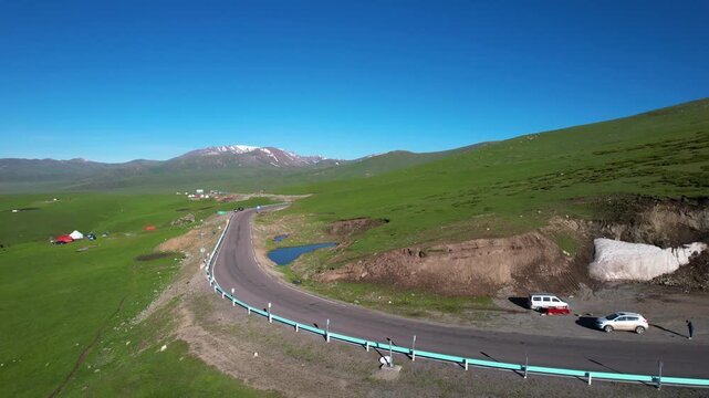 Winding Mountain Road Through Green Valley with Snow Peaks
