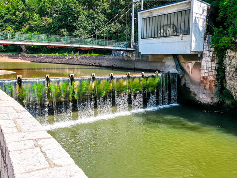 Small dam with flowing water and pedestrian bridge in green urban area. Infrastructure and nature scene in Bosnia and Herzegovina.