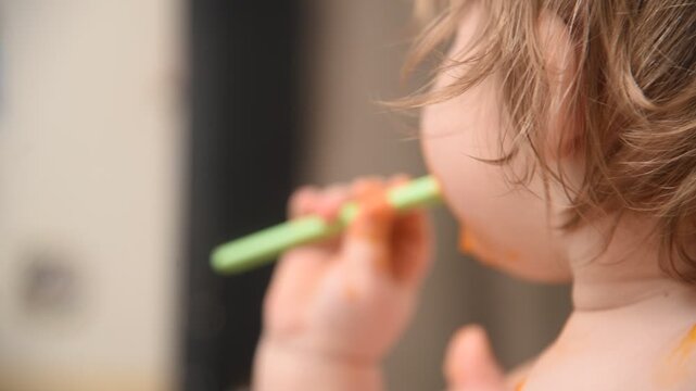  Tender portrait of cute 14-month-old toddler eating vegetable puree with spoon.