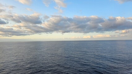 Obraz premium Wide open view of the Atlantic Ocean near Madeira Island with calm blue water and a dramatic cloud-filled sky stretching across the horizon during soft evening light.