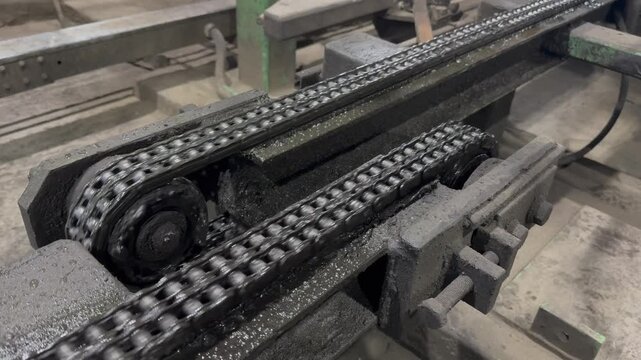 Mechanical drive system in operation, showing a dirty metal roller chain turning gears, heavy industry factory.