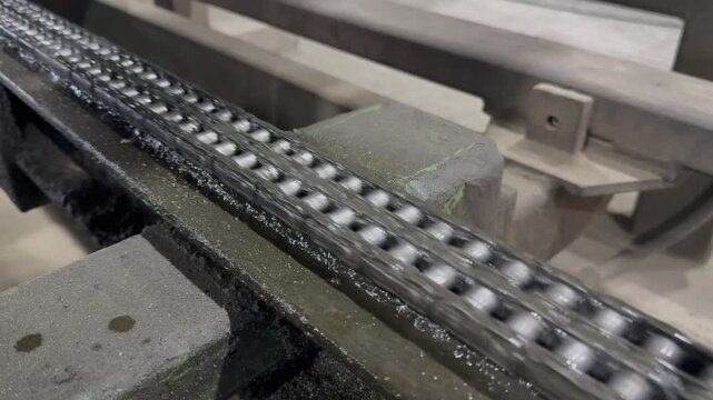 Mechanical drive system in operation, showing a dirty metal roller chain turning gears, heavy industry factory.