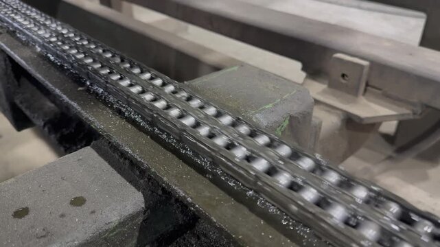 Mechanical drive system in operation, showing a dirty metal roller chain turning gears, heavy industry factory.