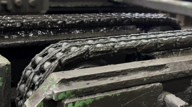 Mechanical drive system in operation, showing a dirty metal roller chain turning gears, heavy industry factory.