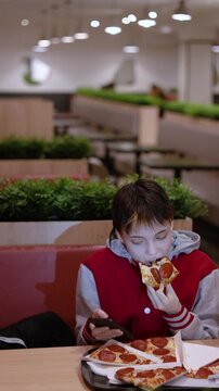 Lost in the digital world, a teenage girl spends her time at a fast food cafe, scrolling endlessly on her phone while eating a slice of warm pizza, oblivious to the bustling world around her.