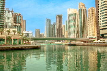Obraz premium Dubai Marina skyscrapers creating a modern skyline, reflecting in the tranquil waters of the canal with a bridge connecting parts of the vibrant urban landscape in United Arab Emirates