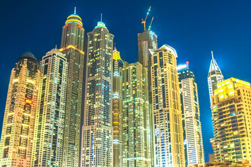 Obraz premium Illuminating Dubai Marina skyline at night, vibrant high-rise towers and glowing lights reflect modern luxury, urban growth and dynamic waterfront architecture in United Arab Emirates