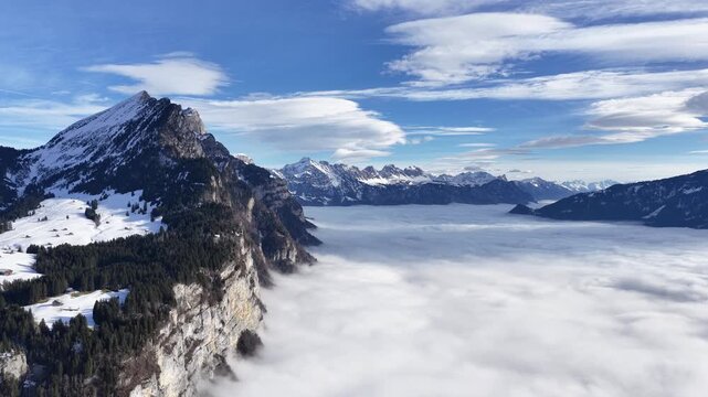 Aerial view above Walensee reveals dramatic cliffs rising from a vast sea of fog, with snow-covered Alpine peaks glowing under crisp winter light.
