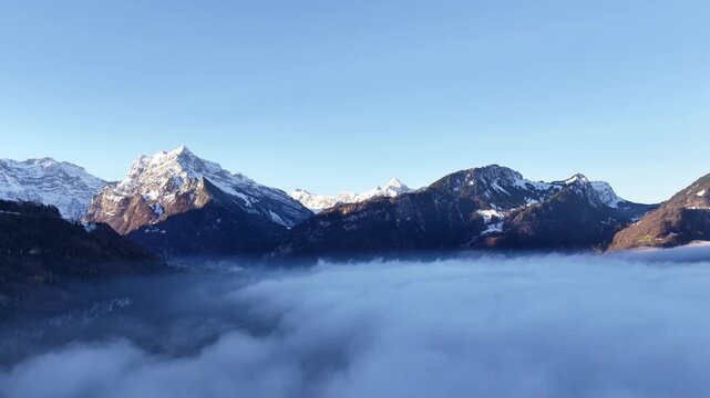 Golden winter sunlight touches distant Alpine peaks while a smooth blanket of fog covers the Walensee lake valley beneath.