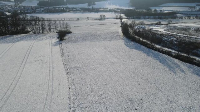 Winter landscape with snow covered countryside fields and rural farmland in Bavaria, Germany. Peaceful cold season nature scenery captured from aerial drone perspective above open terrain.