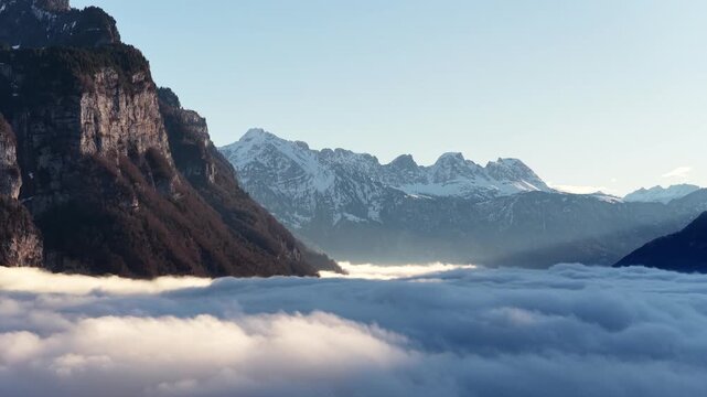 Aerial view of Walensee Lake covered by a dramatic sea of clouds, framed by steep alpine cliffs and distant snowy peaks. Cinematic winter landscape. Concept of serenity and untouched nature.