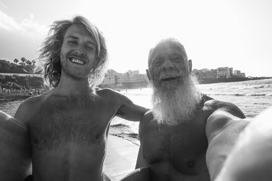 Multigenerational men friends having fun doing selfie on the beach after surf session - Extreme sport and friendship concept - Ugc wide angle lens view content - Main focus on senior male face