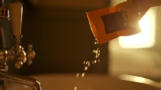 Hand pours spice from packet into sink. Warm light highlights falling granules. Action shot perfect for cooking or seasoning themes. Soft focus on background adds ambiance. Suitable for food, recipe