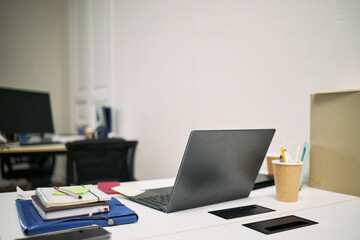 Empty office desk showing closed laptop, stack of documents, stationery, disposable coffee cup, suggesting workspace recently cleaned and organized with no people present