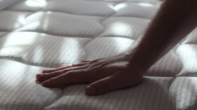 a man strokes a new orthopedic mattress with his hand, assessing the quality before buying in a store, slow motion video