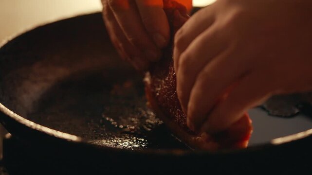 Close-up of hands placing raw steak into hot, oiled skillet. Warm kitchen lighting highlights sizzling meat texture. Steam rises as steak hits surface. Ideal for food blogs, restaurant ads