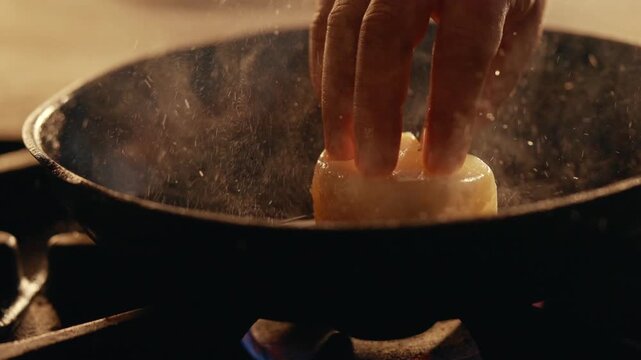 Hand places scallop into hot pan. Steam rises as scallop cooks. Focused action shows careful preparation. Ideal for seafood cooking or restaurant content. High heat sears shellfish for perfect texture