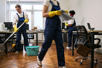 Group of young adult Caucasian man and young adult women cleaning modern office space, wearing...
