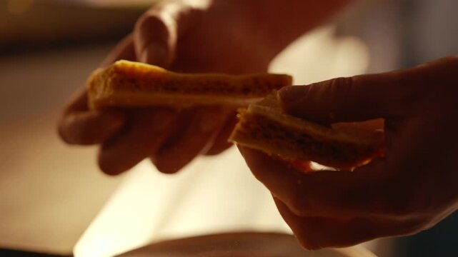 Hands gently break open a toasted sandwich. Warm light highlights golden crusts and melted cheese inside. Scene suggests cozy mealtime or nostalgic comfort food. Perfect for advertising food