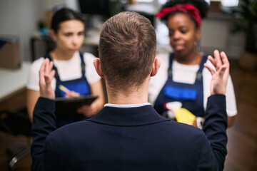 Caucasian middle aged man gesturing while talking to young adult Caucasian woman and young adult...