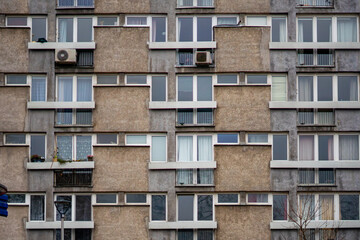Grey facade of a concrete panel apartment block: rows of windows, loggias, balconies and outdoor air conditioning units on a textured building wall – urban residential architecture and social housing. © Adam