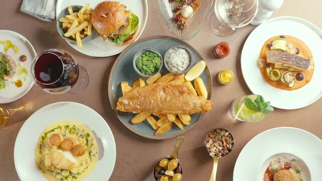 Overhead view of people serving fish and chips on a rustic table. Hands reach for food with casual confidence. Diverse dishes with colorful sides and drinks surround the central plate