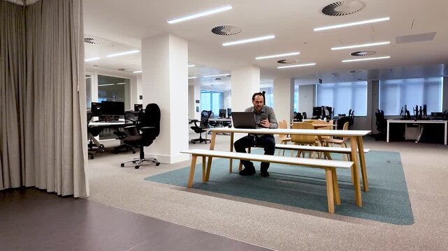 Hybrid Work And Flexible Office Space Lone South Asian Male Working At Table With Laptop And Phone.
