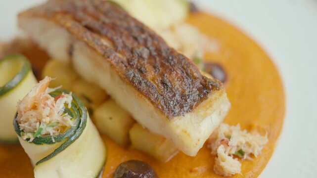 Crispy-skinned fish fillet rests atop vibrant orange sauce. Zucchini rolls and pearl onions add color contrast. Dish looks fresh, gourmet, and perfectly plated. Ideal for food blogs, restaurant menus