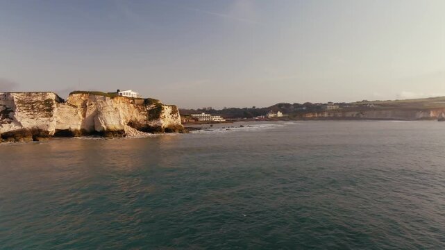 Coastal cliffs rise above calm, turquoise sea under soft sunlight. Cliffs show layered rock formations with sparse vegetation. No people visible in the scene. Footage ideal for travel, nature