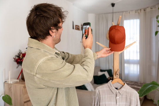 Man photographing a cap with smartphone for online resale, promoting sustainable e-commerce from home