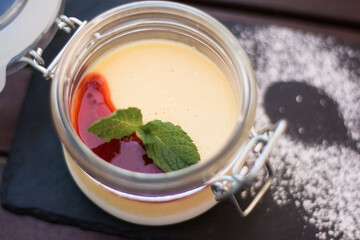 Panna cotta in glass jar with berry sauce and mint leaf. Creamy italian dessert served on slate board with powdered sugar. Sweet gourmet treat for restaurant menu and catering. © Анна Маркина