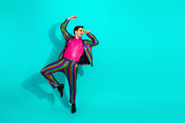 Vibrant retro showman leaps in colorful disco suit with pink shirt and yellow sunglasses against a teal background
