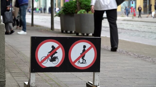 Street sign prohibiting bicycle and scooter riding on pedestrian sidewalk, urban mobility regulation and traffic safety concept. Blurred background.