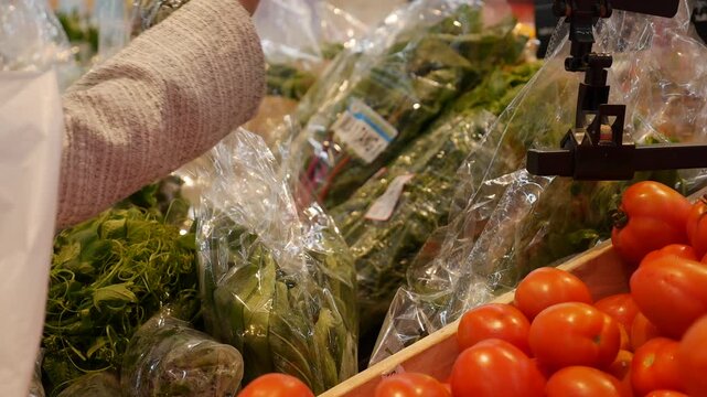 A woman selects fresh leafy greens in the vegetable section of a supermarket, standing near crates filled with produce. Healthy food.