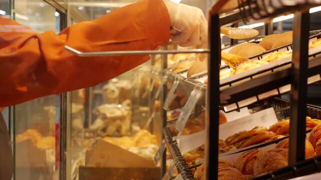 A hand takes baked goods through a glass bakery display window, reaching toward rows of bread and pastries. Fresh bakery.