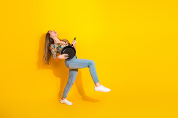 Young woman joyfully jumps with a frying pan against a bright yellow background in a playful...