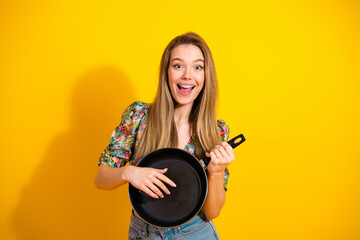 Young stylish woman with frying pan smiling against bright yellow background for fun lifestyle and...