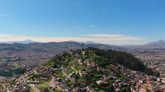 Drone aerial view of El Panecillo hill and the iconic Virgin of Quito statue overlooking the city of Quito, Ecuador, with the Andes mountains and urban landscape in the background.