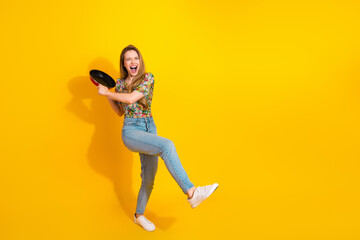 Young stylish woman dancing with a frying pan against a bright yellow background