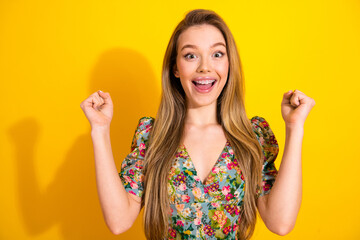 Young woman in floral dress celebrates with joy against bright yellow backdrop