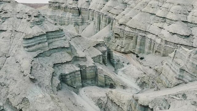 Aerial view of a rugged, rocky terrain with layered sedimentary formations. The landscape appears dry and barren, showcasing natural geological patterns.