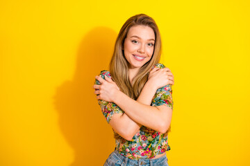 Young woman with floral top hugs herself smiling against bright yellow background
