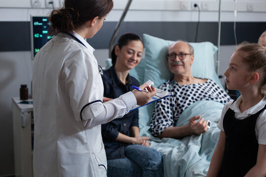 Elderly people care nurse reviewing files of senior male patient bedridden in geriatric hospital. Female general practitioner listening to older hospitalized man symptoms.